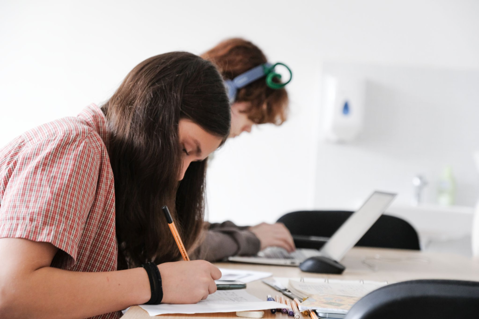 Studentka si píše poznámky do bloku, vedle ní spolužák u notebooku